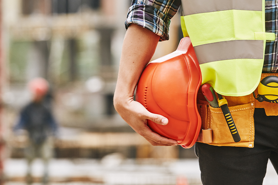 Specialized Business Insurance - Construction worker with Construction Tools Holding a Safety Helmet while Standing Outside at a Construction Site Blurred in the Background